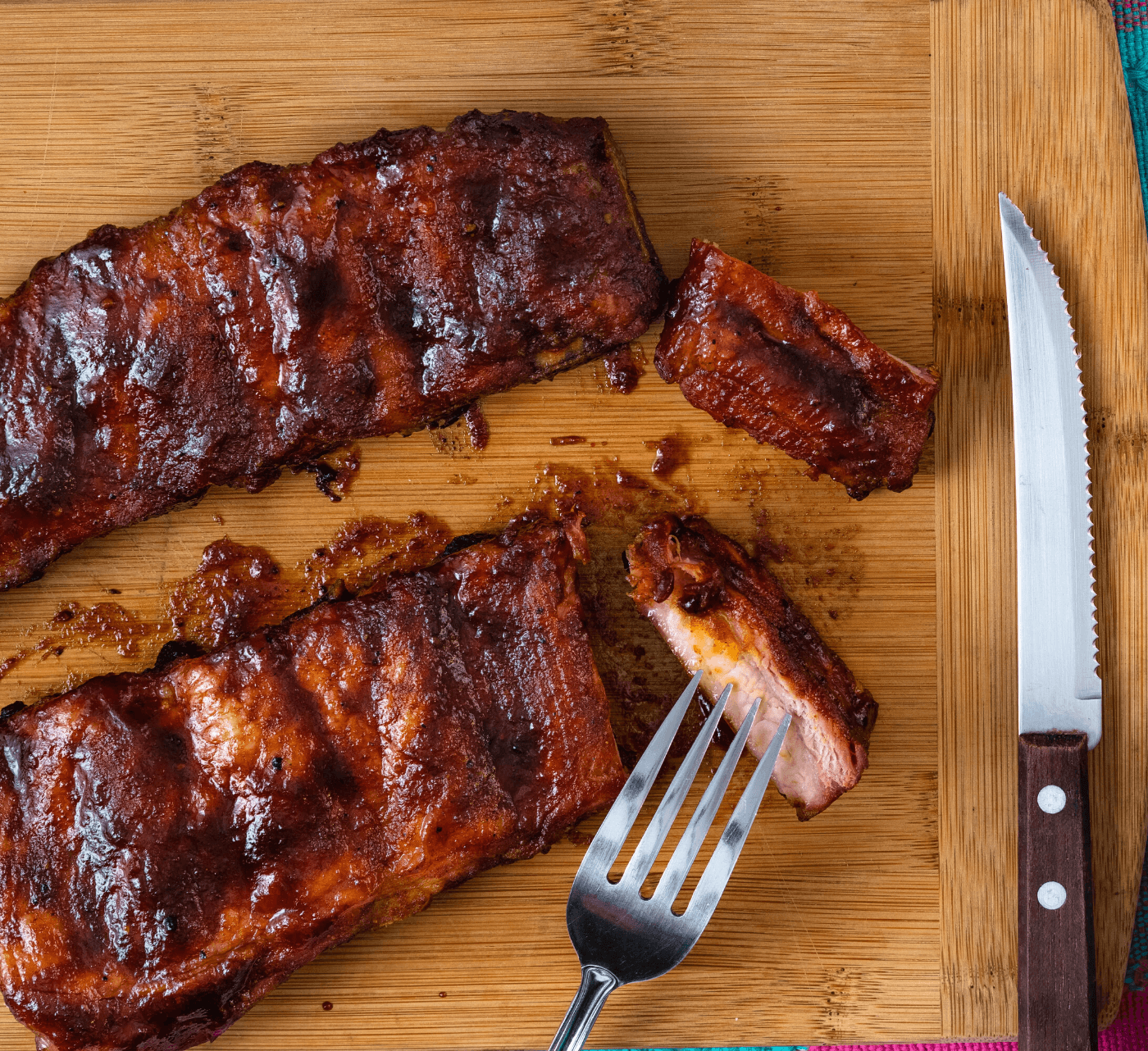 Candied pork ribs on a cutting board with knife and fork.